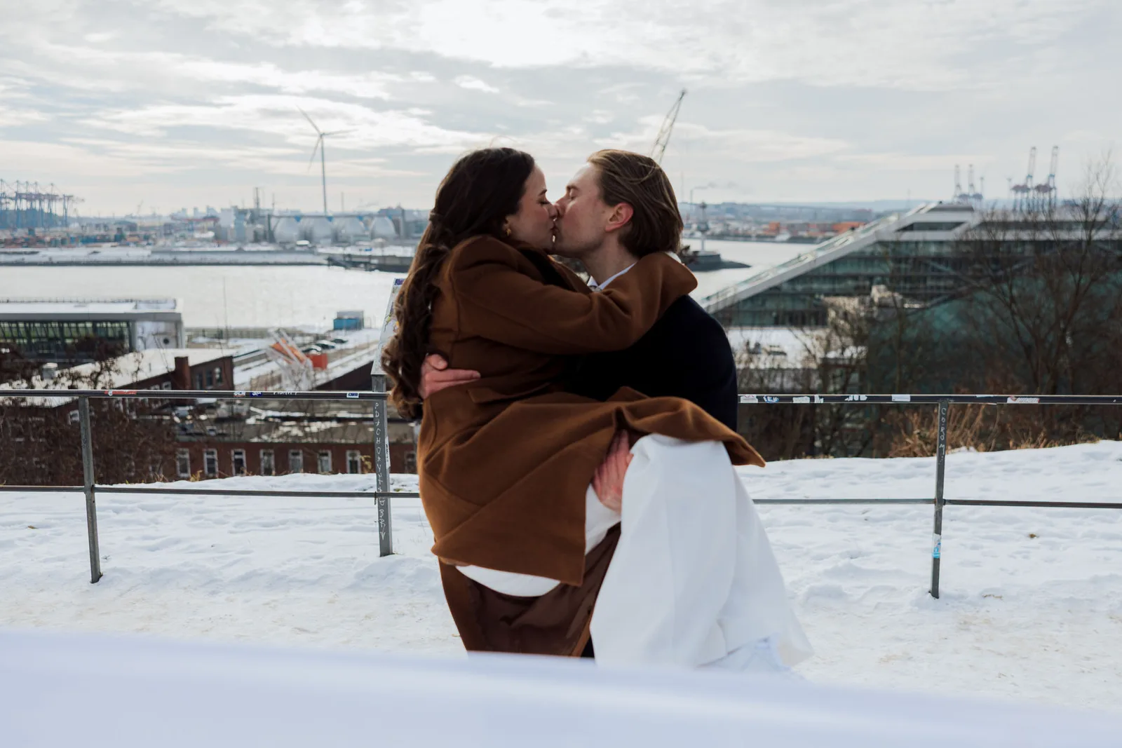 Brautpaar küsst sich im Schnee auf dem Altonaer Balkon, im Hintergrund der Hamburger Hafen